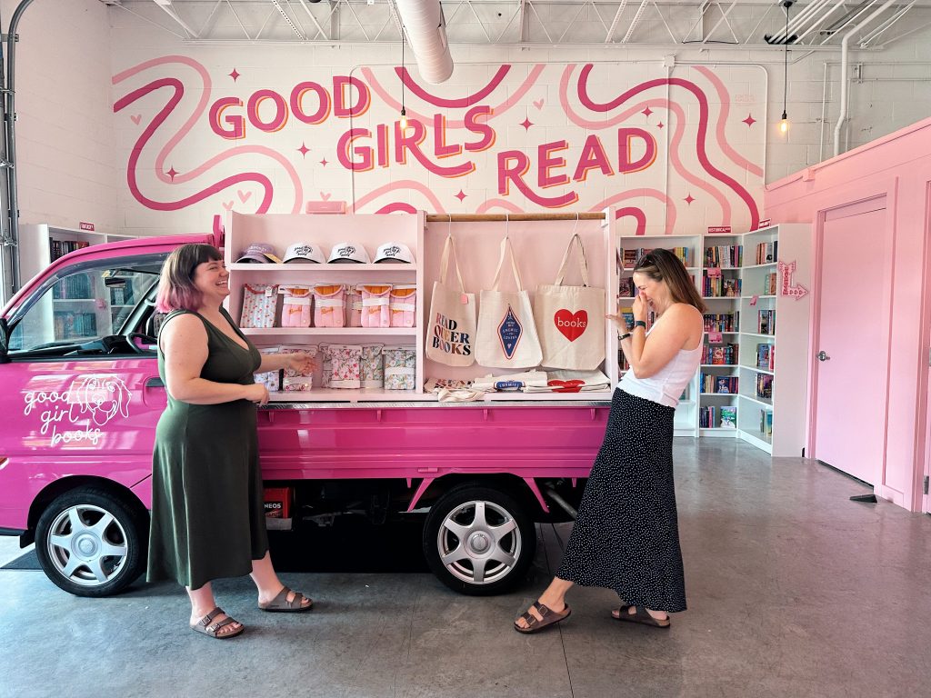 Two women (the owners) stand laughing in front of Little Miss Smuttie at Good Girl Books
